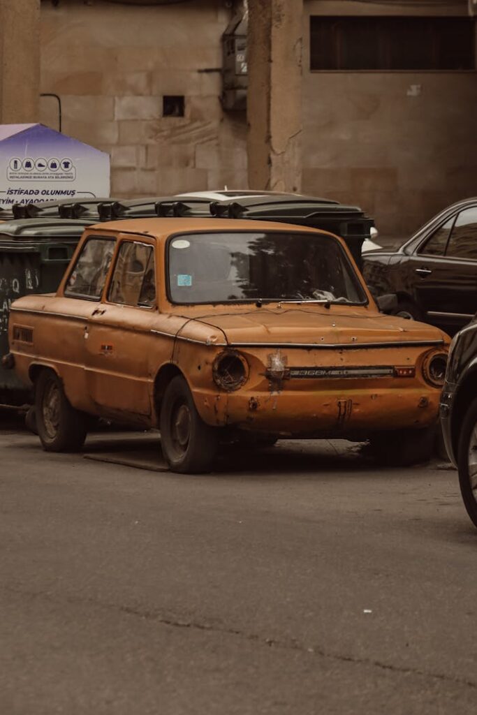 An old, rusty car parked on a street in Baku, capturing urban decay and vintage charm.