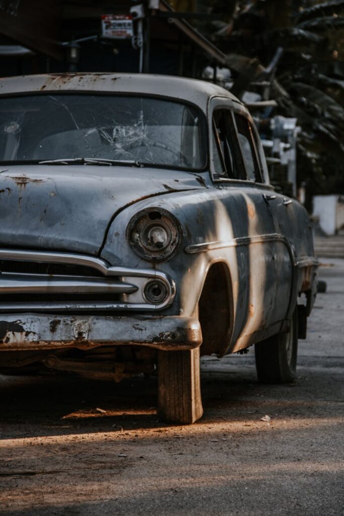 A weathered and rusted vintage car sits abandoned in an urban environment, capturing nostalgic decay.